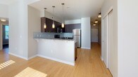 This single-floor residence features a thoughtfully designed open layout that connects the kitchen and living areas seamlessly. The living room is bright and airy, with light wood flooring, neutral-toned walls, and large windows that allow generous natural light to filter in, casting warm patterns across the floor.

The kitchen is a standout space, showcasing rich dark-wood cabinetry that extends to the ceiling for ample storage, complemented by granite countertops with subtle blue-grey tones. A built-in tile backsplash adds texture, while stainless steel appliances—including a refrigerator, range, microwave, and dishwasher—provide a polished, modern aesthetic. A peninsula with pendant lighting overhead offers additional prep space and casual seating.

The bedroom is a calm, carpeted retreat featuring a closet and a sizable window with views of surrounding greenery, filling the room with natural light.

The bathroom is well-appointed with a long granite-topped vanity, dark wood cabinetry with brushed nickel hardware, dual sinks, and a large mirror. A stylish multi-light fixture provides ample illumination, while soft carpeted flooring adds warmth. The overall ambiance of the space is clean, contemporary, and move-in ready.