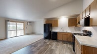 Located at 540 McKinley Ave in Clintonville, Wisconsin, this two-bedroom, one-bathroom unit offers a practical and comfortable single-floor layout. The open-concept kitchen and living room form the heart of the space, with wood-look plank flooring throughout the kitchen area transitioning to plush carpet in the living room. The kitchen is equipped with warm oak cabinetry, light countertops, and a full suite of black appliances including a refrigerator, dishwasher, gas range, and microwave. A sliding glass door in the living area opens to a private balcony, allowing natural light to fill the room. A wall-mounted A/C unit and baseboard heating provide year-round climate control. Both bedrooms feature soft carpeting, ceiling fans, and ample natural light from windows with views of the surrounding area. The primary bedroom includes access to a spacious walk-in closet with built-in shelving and hanging rods for generous storage. An additional bedroom features a bifold closet. The full bathroom offers a single-sink vanity with oak cabinetry, a tub-shower combo, and wood-look flooring consistent with the rest of the unit. A dedicated closet rounds out the storage options in this well-organized and move-in ready space.