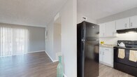 Located at 2002 Colonial Parc Dr in Tampa, FL, this single-floor unit offers a clean, modern aesthetic with a neutral gray color palette and updated luxury vinyl plank flooring carried consistently throughout the space. The open layout connects the living and dining areas seamlessly, with the living room highlighted by a large sliding glass door dressed in vertical blinds that fills the room with abundant natural light. A centrally positioned structural column subtly separates the living area from the kitchen, adding architectural interest. The kitchen is well-appointed with ample white cabinetry, granite-style countertops, a double-basin sink, and black appliances including a full-size refrigerator and an electric range with an overhead exhaust. The bedrooms are comfortably sized with natural light provided by window openings fitted with blinds and textured ceilings overhead. A hallway with light wood-tone flooring and textured walls connects the private areas of the unit, leading to a bathroom featuring a full soaking tub and shower combination with classic white tile surround and a privacy window. Throughout the space, crisp white baseboards and a consistent neutral tone create a cohesive, move-in-ready environment.