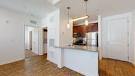 Located at 2098 Seminole Blvd in Largo, Florida, this single-floor residence offers a thoughtfully designed layout with a clean, modern aesthetic throughout. The open-concept living and kitchen area serves as the heart of the unit, where rich wood-style plank flooring extends across the main living spaces, complemented by crisp white walls and abundant natural light filtering through slatted window blinds.

The kitchen is a standout feature, showcasing rich cherry wood cabinetry, a mosaic tile backsplash, and a suite of stainless steel appliances including a refrigerator and built-in microwave. A granite-topped peninsula with pendant lighting overhead provides additional prep space and serves as a natural divider between the kitchen and the main living area.

The living area is generously proportioned, with a tray ceiling detail and a ceiling fan adding both style and comfort. Multiple windows line the walls, creating a bright and airy atmosphere.

The bedroom offers a comfortable retreat, finished with plush wall-to-wall carpeting, a ceiling fan, and a window that allows for natural light. The bathroom is appointed with a rich wood vanity, granite countertop, and a large mirror.

A dedicated in-unit laundry area with a stacked washer and dryer adds everyday convenience, rounding out this functional and well-finished single-floor residence.
