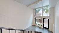 Located in Seattle's vibrant Wallingford neighborhood, this modern two-story home offers a thoughtfully designed layout spread across two floors. The main level features a spacious open-concept kitchen and living area with polished concrete floors that lend an industrial-modern aesthetic. Large windows and a glass door at the entry level flood the space with natural light and provide views of the surrounding greenery, while a private patio extends the living area outdoors. A striking staircase with sleek black metal railings connects the main level to the upper floor, serving as a design focal point.

The upper level houses the generously sized bedroom, complete with plush carpeting, two well-appointed closets featuring wire shelving systems for ample storage, and convenient access to a full bathroom with a stacked washer and dryer unit integrated directly into the space — combining laundry and bath functions efficiently. Wood-look flooring in this bathroom adds warmth alongside a modern vanity with a clean white countertop. A second bathroom on the main level provides additional convenience for guests. The home's clean white walls, recessed lighting throughout, and contemporary finishes create a bright, cohesive, and functional living environment.