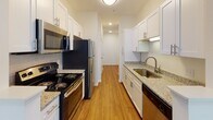 Located at 2004 Calvary Circle in Charlottesville, Virginia, this single-floor residence offers a well-designed layout with a clean, neutral aesthetic throughout. The open living area features plush carpeting, crown molding, and a ceiling fan, and connects seamlessly to a galley-style kitchen via a pass-through opening. The kitchen is outfitted with white shaker-style cabinetry, granite countertops, a stainless steel sink, and appliances including an electric range, built-in microwave, refrigerator, and dishwasher, all complemented by warm hardwood-style flooring and subway tile backsplash. The bedrooms are carpeted and generously sized, each equipped with ceiling fans. One bedroom features a large walk-in closet with built-in shelving, while another benefits from bright, tree-lined window views that bring natural light into the space. The bathroom includes a wide vanity with granite countertops, white cabinetry, a large mirror with contemporary lighting, and a tiled tub-shower combination. Throughout the residence, windows dressed with horizontal blinds provide views of the surrounding greenery, contributing to a bright and airy atmosphere. The consistent use of white walls and neutral finishes creates a cohesive, move-in-ready environment.
