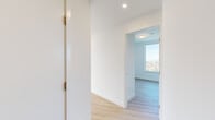 This thoughtfully designed unit offers four bedrooms and two bathrooms across a single floor, presenting a clean, contemporary aesthetic throughout. Light-toned hardwood flooring flows seamlessly from room to room, complementing the crisp white walls and recessed lighting that give the entire space a bright, airy character.

The kitchen is a standout feature, boasting a large white quartz island with an undermount sink, flat-front cabinetry in both white and warm wood tones, stainless steel appliances, and a tile backsplash. Floor-to-ceiling windows frame sweeping panoramic views of a treetop canopy and city skyline beyond, flooding the kitchen with abundant natural light.

The four bedrooms maintain the unit's minimalist tone, each finished with the same light hardwood flooring and white walls. Several bedrooms include built-in sliding-door closets, while the primary bedroom offers a compact, well-proportioned layout. A connecting hallway links the bedrooms efficiently to the rest of the unit.

The two bathrooms are finished with modern fixtures and warm wood vanity cabinetry topped with white countertops. One bathroom features a frameless sliding glass shower enclosure, while the second offers a full soaking tub with overhead shower. Both maintain the clean, understated design language found throughout the space.