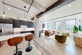 Located in the heart of downtown Tulsa at 410 S Boulder Ave, this modern loft-style residence blends industrial character with contemporary finishes across four bedrooms and two bathrooms. The open-concept main living area immediately impresses with exposed concrete columns, dark wood ceiling beams, and polished terrazzo flooring that transitions seamlessly between the kitchen and living room. The kitchen is outfitted with matte navy cabinetry, stainless steel appliances, a light wood island with a white quartz countertop, and pendant globe lighting — ideal for both cooking and casual dining. The living room offers abundant natural light through large black-framed windows and features track lighting overhead. The bedrooms are bright and well-proportioned, with large windows framing views of the surrounding Tulsa cityscape and tree canopy. Several bedrooms include ceiling fans and stylish barn-style sliding doors. The bathrooms feature frameless glass shower enclosures and polished concrete flooring. A dedicated laundry area with a full-size GE Profile washer completes the layout. Throughout, the design strikes a refined balance between industrial loft aesthetics and modern residential comfort, making this a distinctive urban residence.