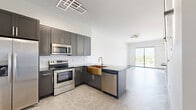 Located at 2750 Griffin Rd in Dania Beach, FL, this thoughtfully designed one-bedroom, one-bathroom unit offers a contemporary living experience across a single floor. The open-concept layout seamlessly connects the kitchen, dining, and living areas, creating a spacious, airy feel filled with natural light. The kitchen is a standout feature, outfitted with charcoal-toned shaker cabinets with gold hardware, dark granite countertops, a striking gold farmhouse sink, white subway tile backsplash, and a full suite of stainless steel appliances. A geometric LED light fixture adds a modern, architectural touch overhead. Polished concrete-style floors flow throughout, lending the space an industrial-chic aesthetic. The living area opens directly to a private balcony through large sliding glass doors, offering outdoor views of the surrounding Dania Beach neighborhood. The bedroom is a calm, well-proportioned retreat featuring a full-width closet with sleek panel doors and its own balcony access. A dedicated office provides flexible space for work or study. The bathroom is finished in a clean, modern style with large-format white tile, a glass-enclosed walk-in shower with a rain showerhead, matte black fixtures, and an illuminated vanity mirror.