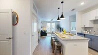 Located at 3701 Southwest 34th Street in Gainesville, FL, this well-appointed 2-bedroom, 2-bathroom unit offers a thoughtfully designed single-floor layout with a clean, modern aesthetic throughout. The open-concept kitchen serves as the heart of the home, featuring sleek white upper cabinetry, contrasting gray lower cabinets, a subway tile backsplash, stainless steel appliances, and a generous granite-topped island with seating for multiple guests — illuminated by striking black pendant lights overhead. Light wood-style flooring flows seamlessly from the kitchen into the living room, which is anchored by a ceiling fan and a set of French doors that flood the space with natural light and provide access to an outdoor area. Both bedrooms are carpeted and bright, each offering large windows with outdoor views and dedicated closets with wire shelving systems for ample storage. The bathrooms are finished with granite vanity countertops, dark cabinetry, and full soaking tubs with tiled surrounds. The primary bedroom is generously sized with its own en-suite bath. Throughout the unit, crisp white walls, recessed lighting, and consistent finishes create a cohesive and inviting atmosphere.