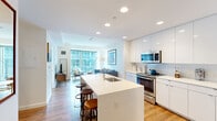 Located at 1335 Boylston St in Boston's vibrant Fenway neighborhood, this well-appointed one-bedroom, one-bathroom unit offers a thoughtfully designed open-concept layout. The kitchen is a standout feature, showcasing sleek white high-gloss cabinetry, a full suite of stainless steel appliances including a French door refrigerator, electric range, microwave, and dishwasher, complemented by a white quartz waterfall island with bar seating — ideal for casual dining or entertaining. The kitchen flows seamlessly into the living area, where large floor-to-ceiling windows flood the space with natural light and provide views of the surrounding Boston cityscape. Warm hardwood flooring runs throughout, creating a cohesive and inviting atmosphere. The bedroom is a comfortable retreat, featuring a closet, hardwood floors, and large windows that continue the theme of natural light and urban views. The bathroom is finished with large-format floor tiles, a sleek glass-enclosed walk-in shower with full-height tile surround, and clean, modern fixtures. Recessed lighting throughout the unit enhances the bright, contemporary aesthetic, making this a refined urban residence in one of Boston's most sought-after locations.