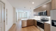 Located at 1455 Moonrise Avenue in Carrollton, TX, this well-appointed one-bedroom, one-bathroom residence offers a thoughtfully designed single-floor layout with modern finishes throughout. The open-concept kitchen serves as the heart of the home, featuring warm wood-toned cabinetry, crisp white quartz countertops, a white subway tile backsplash, and a peninsula with an undermount sink. A full suite of stainless steel appliances includes a side-by-side refrigerator with ice and water dispenser, an electric range, built-in microwave, and dishwasher. Stylish pendant lighting hangs above the peninsula, adding a contemporary touch. Light hardwood-style flooring extends throughout the main living area and bathroom, creating a cohesive and clean aesthetic. The living area receives natural light through windows fitted with horizontal blinds. The bedroom is carpeted for comfort, offers ample natural light from multiple windows with blinds, and includes a ceiling fan. A walk-in closet with built-in shelving and hanging rods provides generous storage. The bathroom features matching wood-toned cabinetry, a white countertop vanity, and wood-style flooring, with direct access to the walk-in closet. Recessed lighting and a neutral color palette throughout contribute to a bright, modern ambiance.