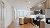 This compact yet well-appointed 540 square foot apartment in Carrollton, Texas, offers a harmonious blend of functionality and style. The single-floor layout comprises one bedroom, one bathroom, and an open-concept living area. The kitchen is a standout feature, boasting sleek wood-grain cabinetry, stainless steel appliances including a side-by-side refrigerator, built-in microwave, and electric range. A white subway tile backsplash and quartz countertops add a touch of elegance.

The living area seamlessly connects to the kitchen, creating an airy feel enhanced by recessed lighting and pendant fixtures. Warm wood-look flooring runs throughout the main living spaces, while the bedroom features plush carpeting for comfort. Large windows with horizontal blinds allow ample natural light, brightening the neutral-toned walls.

The bathroom continues the modern aesthetic with a wooden vanity, white countertop, and ample storage. A combination of wood flooring and tile adds visual interest. The bedroom, measuring 120 square feet, includes a closet with built-in shelving for organized storage. A ceiling fan provides additional comfort. Despite its modest size, this apartment efficiently utilizes every square foot, creating a cozy yet functional living space.