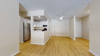This single-floor residence offers a clean, functional layout with a thoughtfully designed open-concept living and kitchen area. The kitchen is well-appointed with white shaker-style cabinetry, granite countertops, and a full suite of stainless steel appliances, including a refrigerator, electric range, over-the-range microwave, and dishwasher. A peninsula-style counter divides the kitchen from the open living space, providing additional workspace and a natural gathering point. Light hardwood-style flooring runs throughout the main living areas, lending warmth and continuity to the space, while a ceiling fan overhead adds both function and comfort to the living room. The bedroom features plush carpeting, a wall-mounted air conditioning unit, baseboard heating, and a window that invites natural light and an exterior view. Closet space is generously provided, with bifold-door closets visible in the sleeping area. The bathrooms are finished with white cabinetry, granite vanity countertops, light wood-style flooring, and a tiled tub-and-shower combination. A textured ceiling throughout adds a traditional touch. Overall, the space presents a bright, neutral palette that offers a comfortable and practical living environment.