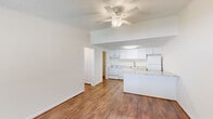 This single-story, one-bedroom, one-bathroom unit offers a thoughtfully arranged floor plan that maximizes its compact footprint. Warm hardwood-style flooring runs throughout the space, creating a cohesive and inviting atmosphere from room to room.

The living area is bright and open, featuring a ceiling fan with a light fixture and a textured ceiling. A large window allows natural light to fill the room while providing an outdoor view, and a wall-mounted heating unit sits beneath it. The living area flows directly into the kitchen, which is designed with white shaker-style cabinetry extending to the ceiling, granite-look countertops, and a peninsula that adds additional prep and dining space. White appliances include a range, dishwasher, and refrigerator, complemented by an overhead exhaust hood.

The bedroom is a comfortable size, featuring a wide louvered bi-fold closet, a ceiling fan, natural light from a window, and crown molding details. The full bathroom includes a combined tub and shower, a vanity with an integrated sink, and a large mirror. A dedicated utility room and hallway with a louvered closet door complete the layout.