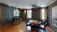 Located at 1315 W St NW in Washington, DC's dynamic U Street neighborhood, this single-floor entertainment space delivers a refined yet relaxed atmosphere through a thoughtful blend of upscale design elements and versatile amenities.

The lounge area is anchored by a striking dark marble fireplace flanked by warm walnut built-in shelving against bold chevron-patterned wallcovering. A plush seating arrangement — including a tufted sofa and accent chairs — surrounds a circular glass coffee table, while large windows with draped curtains invite natural light and street-level views of the surrounding neighborhood.

Adjacent to the lounge, the game room features a full-sized pool table set on rich hardwood flooring, complemented by a foosball table and additional entertainment options. The wet bar area is outfitted with dark granite countertops, white cabinetry, a stainless steel sink, and a wall-mounted flat-screen television, offering a functional and stylish hub for hosting.

The poker lounge showcases exposed brick walls, warm hardwood floors, and abundant natural light from multiple windows framed by floor-length draping curtains. A dedicated poker table with leather seating and a high-top bar table complete this well-appointed gaming area. Curated artwork and accent lighting throughout contribute to the space's sophisticated, club-like ambiance.