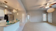 This well-designed one-bedroom, one-bathroom unit in Oklahoma City, Oklahoma offers a practical and comfortable single-floor layout. The open-concept kitchen and living area forms the heart of the space, where light tile flooring transitions seamlessly into plush wall-to-wall carpeting. The kitchen is outfitted with white shaker-style cabinetry, stainless steel appliances including a refrigerator, range, microwave, and dishwasher, and a butcher-block-topped peninsula that doubles as a dining surface. Two stylish Edison bulb pendant lights hang above the peninsula, adding a warm, modern touch. Track lighting above the kitchen provides additional task illumination. The open living area is generously sized, featuring a ceiling fan and access to a private entry door, with multiple windows that allow natural light to fill the room. The spacious bedroom is carpeted and includes a ceiling fan, windows with exterior views, and ample room for furnishings. The bathroom features a dual-sink vanity with white cabinetry, a large mirror, and modern light fixtures, complemented by tile flooring and access to a dedicated closet. Neutral gray tones throughout create a cohesive, contemporary aesthetic.