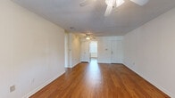 This single-floor unit showcases a thoughtful blend of classic and functional design elements throughout its layout. The open living area is anchored by warm hardwood flooring that extends through the main living spaces, complemented by white walls and ceiling fans that contribute to a bright, airy atmosphere. A striking painted brick accent wall adds architectural character to both the living area and kitchen, where it frames a large window fitted with vertical blinds that allows natural light to pour in. The kitchen is equipped with stainless steel appliances, wood cabinetry, and tile backsplash, offering a practical and well-appointed cooking space. The bedrooms are carpeted for comfort and feature the same exposed brick detailing alongside windows that bring in natural light. One bedroom includes generously sized louvered bi-fold closet doors, providing substantial storage. The bathroom is well-finished, featuring a tiled tub-shower combination, a wood-framed vanity with a dark granite countertop, a basin sink, and a large mirror. Ceiling fans are present throughout, enhancing comfort across all rooms. The overall ambiance is clean, neutral, and functional.