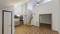 This two-floor residence offers a thoughtfully designed layout with standout architectural details throughout. The main level is anchored by a spacious living area with dramatic vaulted ceilings that amplify the sense of openness and airiness. A tiled wood-burning fireplace serves as a focal point in the living room, complemented by wood-style plank flooring that extends throughout the main living areas. Natural light filters in through multiple windows, enhancing the bright, clean aesthetic of the white walls.

The kitchen is well-appointed with sage-green cabinetry, granite-style countertops, and a full suite of stainless steel appliances including a range, over-the-range microwave, dishwasher, and refrigerator. A pendant light fixture adds a finishing touch above the kitchen area. A staircase with a wood handrail leads to the upper level, where a loft-style space features sloped ceilings, carpet flooring, a ceiling fan, and an open railing overlooking the main floor below.

The bathrooms are finished with matching grey cabinetry and granite-style countertops. One full bathroom includes a soaking tub with a tiled surround and grab bars, while a second bathroom features a standalone shower with a frosted glass door. Additional rooms offer dark hardwood-style flooring and ample space for flexible use.