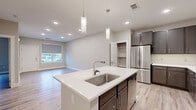 This single-floor unit is designed with a clean, contemporary aesthetic that emphasizes functionality and modern finishes. Light wood-look flooring runs consistently throughout the living areas, complementing the neutral warm-beige wall tones and crisp white baseboards that frame each room.

The kitchen serves as the centerpiece of the open-concept living space, featuring a large center island with a white quartz countertop, an undermount stainless steel sink, and two pendant lights overhead. Dark espresso-toned cabinetry extends along the walls, providing ample storage, and is paired with a full suite of stainless steel appliances including a French door refrigerator, electric range, microwave, and dishwasher. An adjacent open pantry adds additional storage convenience.

The bedrooms are well-proportioned, each featuring windows with roller shades that allow natural light and outdoor views. The primary bathroom offers a dual-sink vanity with backlit mirrors, white quartz countertops, dark cabinetry, and a glass-enclosed walk-in shower.

Additional highlights include a dedicated laundry area with a stacked washer and dryer unit, recessed lighting throughout, and an attached garage with an automatic opener, providing secure and direct access to the unit.
