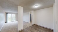 This two-bedroom, one-bathroom residence in Portland, Oregon offers a practical and well-organized single-level layout. The combined living and dining area is a welcoming, open space finished with plush carpeting and a textured ceiling, with a sliding glass door that leads to a private balcony overlooking a green outdoor area, filling the room with natural light. Structural columns define the transition between the living space and the kitchen, which features wood-look hardwood-style flooring, gray shaker-style cabinetry, light quartz countertops, a stainless steel sink, and a window that brightens the workspace. A hallway connects the living areas to the two carpeted bedrooms, each offering a quiet retreat with windows providing natural light and baseboard heating. Both bedrooms include closets with shelving, and the primary bedroom features a spacious walk-in style closet. The full bathroom is finished with wood-look tile flooring, a gray vanity, and a tub-shower combination. Three closets throughout the unit provide ample storage. The neutral color palette and clean finishes throughout create a move-in ready environment well-suited for comfortable everyday living in North Portland.