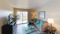 This single-story residential unit is designed with a practical, well-organized layout that connects living, sleeping, and functional spaces cohesively. Rich dark hardwood-style flooring runs consistently throughout, providing a warm, grounding contrast to the neutral beige wall tones present in every room.

The living room serves as the central gathering space, featuring a sliding glass door framed by vertical blinds that opens to a private balcony, allowing natural light to fill the room. A sectional sofa, glass coffee table, and a media console furnish the space comfortably, with a patterned area rug adding a pop of teal color.

The kitchen follows a galley-style configuration with white cabinetry, white appliances including an electric range and refrigerator, and overhead lighting. Its efficient layout maximizes use of the available space.

The bedrooms are well-proportioned, each featuring large sliding-door closets offering generous built-in storage. Windows fitted with vertical blinds provide natural light, and the neutral walls create a calm, restful atmosphere.

The bathroom includes a vanity with a large mirror, white cabinetry for storage, and a bathtub-shower combination. Consistent dark flooring ties the bathroom seamlessly to the rest of the unit, reinforcing a unified design throughout.