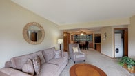 This single-floor space offers a well-organized layout designed for comfortable everyday living. The living room serves as the central gathering area, finished with plush carpeting and neutral walls that create a warm, inviting atmosphere. A large sliding glass door fills the space with natural light and provides views of the surrounding exterior. A decorative round mirror with a woven wood frame accents one wall, complementing the understated, cozy aesthetic.

The living area flows seamlessly into the dining space, which features a standout built-in shelving unit with a teal-painted interior backdrop—a distinctive design element that adds a pop of color and visual interest. A ceiling fan overhead provides both function and a focal point in this area. Adjacent to the dining space is the kitchen, equipped with warm oak cabinetry, black appliances including a range, over-the-range microwave, and dishwasher, as well as durable wood-look flooring and light countertops.

Two bedrooms offer comfortable retreats, each carpeted and featuring windows that allow natural light. The full bathroom includes a tub and shower combination with sliding glass doors, tile flooring, and an oak vanity, while a second bathroom provides additional convenience. The overall design balances functionality with a warm, residential character throughout.