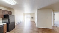 This single-floor unit offers a functional and practical layout across several well-defined spaces. The open living area is finished with wood-style laminate flooring and features a textured ceiling, baseboard heating, and a wall-mounted air conditioning unit. A sliding glass door fitted with vertical blinds allows natural light to fill the space and provides outdoor access.

The kitchen is well-appointed with rich, dark wood cabinetry offering generous storage, light-toned countertops, and a full suite of black appliances including an electric range, microwave, dishwasher, and refrigerator. A skylight overhead supplements the natural light. The kitchen connects conveniently to an exterior entry door.

The bedrooms are carpeted for comfort, each featuring windows that bring in natural light, baseboard heating, and closet storage. One room includes a built-in wire shelving system and houses in-unit laundry, adding everyday convenience.

The bathroom is finished with wood-style flooring and includes a vanity with a granite-style countertop, dark cabinetry, a wall mirror, and a tub-shower combination. Neutral wall tones throughout the unit create a clean, cohesive aesthetic.