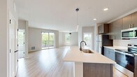 Located at 8421 Mansion Hill Ave in Madison, Wisconsin, this thoughtfully designed 2-bedroom, 2-bathroom residence offers a clean, modern aesthetic across a single well-appointed floor. The open-concept living and kitchen area serves as the heart of the home, anchored by light-toned hardwood-style flooring that flows seamlessly throughout. The kitchen is a standout feature, equipped with stainless steel appliances, dark wood cabinetry extending to the ceiling, light quartz countertops, and a large center island with a built-in sink and pendant lighting — ideal for both cooking and entertaining. The dining area is accented by a modern dome pendant light and a large window that fills the space with natural light. The living room opens directly onto a private balcony through sliding glass doors, offering picturesque views of the surrounding mature trees. Both bedrooms feature plush carpet, ceiling fans, and generous windows that invite ample natural light. The primary bedroom includes its own closet and an en suite bathroom featuring a long wood-toned vanity, illuminated mirror, walk-in tiled shower with a sleek black-framed glass door, and light hardwood flooring. The second bathroom offers a full soaking tub and shower combination with clean white finishes and matching black hardware accents. Two closets provide practical storage throughout the home.