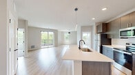 Located at 8421 Mansion Hill Ave in Madison, Wisconsin, this thoughtfully designed 2-bedroom, 2-bathroom residence offers a clean, modern aesthetic across a single well-appointed floor. The open-concept living and kitchen area serves as the heart of the home, anchored by light-toned hardwood-style flooring that flows seamlessly throughout. The kitchen is a standout feature, equipped with stainless steel appliances, dark wood cabinetry extending to the ceiling, light quartz countertops, and a large center island with a built-in sink and pendant lighting — ideal for both cooking and entertaining. The dining area is accented by a modern dome pendant light and a large window that fills the space with natural light. The living room opens directly onto a private balcony through sliding glass doors, offering picturesque views of the surrounding mature trees. Both bedrooms feature plush carpet, ceiling fans, and generous windows that invite ample natural light. The primary bedroom includes its own closet and an en suite bathroom featuring a long wood-toned vanity, illuminated mirror, walk-in tiled shower with a sleek black-framed glass door, and light hardwood flooring. The second bathroom offers a full soaking tub and shower combination with clean white finishes and matching black hardware accents. Two closets provide practical storage throughout the home.