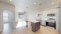 Located at 9990 E Harvard Ave in Denver, CO, this modern residence offers a thoughtfully designed layout across a single floor. The open-concept living and kitchen area serves as the heart of the home, featuring light hardwood flooring, recessed lighting, and a ceiling fan that enhances airflow throughout the space. Large sliding glass doors flood the living area with natural light and provide outdoor views, creating a bright and welcoming atmosphere.

The kitchen is well-appointed with stainless steel appliances, including a full-size refrigerator, range, microwave, and dishwasher. Two-tone cabinetry — white uppers paired with dark lower cabinets — offers generous storage, while a central island with an attached dining table provides versatile space for meal prep and casual dining.

Three bedrooms are accessible via a clean, light-filled hallway. The primary bedroom features a ceiling fan and sliding glass door access to an outdoor area, while the secondary bedrooms include large windows with blinds, ceiling fans, and ample closet space.

The shared bathroom is finished in a modern style with a white subway tile tub/shower surround, a clean vanity with dark cabinetry and white countertop, and a round mirror. Light hardwood flooring is carried throughout, tying the entire residence together with a cohesive, contemporary aesthetic.