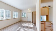 This well-designed one-bedroom, one-bathroom unit offers a practical and comfortable single-floor layout. Light wood-style flooring runs throughout the entire space, lending a clean, cohesive look to every room.

The living room is one of the most notable areas, featuring three large windows fitted with white horizontal blinds that invite an abundance of natural light and views of the surrounding greenery. The bright, neutral walls enhance the sense of openness in this comfortable gathering space.

The kitchen is thoughtfully laid out in a U-shaped configuration, maximizing counter and storage space. Light wood cabinetry—both upper and lower—provides generous storage, while white appliances including a refrigerator, electric range, and dishwasher complete the functional setup. A separate countertop area serves well as a breakfast bar or additional prep space.

The bedroom offers a comfortably sized retreat with a large window providing natural light and an outdoor view, along with dual sliding-door closets that deliver ample storage capacity.

The bathroom includes a combined tub and shower, a vanity with storage, and a clean, straightforward layout. Throughout the unit, the consistent use of warm neutral tones, light flooring, and well-placed windows creates a bright, welcoming atmosphere.
