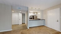 This single-story unit located in Norcross, Georgia, offers a well-organized layout designed for comfortable everyday living. The open-concept kitchen is a central highlight, featuring white shaker-style cabinetry, a subway tile backsplash, stainless steel appliances including a range and refrigerator, and dark countertops that extend across a peninsula with an integrated sink. Pendant lighting overhead adds a polished touch, while the pass-through design connects seamlessly to the adjoining living area.

The living space is carpeted in a warm neutral tone and benefits from natural light through a sliding glass door fitted with vertical blinds, which opens to an outdoor area with views of surrounding greenery. A secondary bedroom features a window with blinds and plush carpet, providing a quiet, functional space. The primary bedroom is generously proportioned with carpeted flooring, a walk-in closet, and access to an additional closet area for ample storage.

The bathroom includes a dark-toned vanity countertop, a large mirror, wood-look flooring, and a tiled shower-tub combination. Throughout the unit, textured ceilings, neutral wall tones, and consistent finishes create a cohesive, understated ambiance.