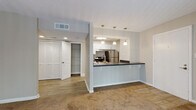 This single-story unit located in Norcross, Georgia, offers a well-organized layout designed for comfortable everyday living. The open-concept kitchen is a central highlight, featuring white shaker-style cabinetry, a subway tile backsplash, stainless steel appliances including a range and refrigerator, and dark countertops that extend across a peninsula with an integrated sink. Pendant lighting overhead adds a polished touch, while the pass-through design connects seamlessly to the adjoining living area.

The living space is carpeted in a warm neutral tone and benefits from natural light through a sliding glass door fitted with vertical blinds, which opens to an outdoor area with views of surrounding greenery. A secondary bedroom features a window with blinds and plush carpet, providing a quiet, functional space. The primary bedroom is generously proportioned with carpeted flooring, a walk-in closet, and access to an additional closet area for ample storage.

The bathroom includes a dark-toned vanity countertop, a large mirror, wood-look flooring, and a tiled shower-tub combination. Throughout the unit, textured ceilings, neutral wall tones, and consistent finishes create a cohesive, understated ambiance.