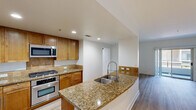 This single-floor, 3-bedroom, 2-bathroom residence offers a thoughtfully designed layout that balances functionality and modern style. Light wood-style flooring flows consistently throughout the home, creating a clean, cohesive aesthetic. The open-concept kitchen and living area serves as the heart of the space, featuring warm-toned wooden cabinetry, granite countertops with stone-patterned detailing, and a full suite of stainless steel appliances including a gas range, built-in microwave, and French door refrigerator. A peninsula with an undermount sink and a professional-style faucet provides additional prep space and a natural transition into the living area. The primary bedroom is generously proportioned and opens via sliding glass doors to a private balcony with outdoor views. The primary bathroom is well-equipped with a glass-enclosed walk-in shower, a separate soaking tub, a granite-topped vanity, and a backlit mirror. The secondary bathroom mirrors the same design language with a granite vanity, wooden cabinetry, and a tub-shower combination. The additional bedrooms are bright and airy, with large windows that invite natural light. Each bedroom includes closet space with built-in rods for storage. Recessed lighting throughout maintains a clean, modern look.