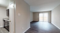 This single-story, one-bedroom, one-bathroom unit offers a functional and cohesive layout designed to maximize its comfortable footprint. Throughout the space, wood-style flooring in rich, warm tones provides a consistent and polished look, complementing the neutral greige wall palette found in every room.

The open living area serves as the heart of the unit, featuring a sliding glass door dressed with vertical blinds that invites natural light and provides access to an outdoor area. The living space flows seamlessly toward the entry and connects to the galley-style kitchen, which is separated by a partial wall. The kitchen is equipped with dark espresso cabinetry extending from floor to ceiling, granite-style countertops, and black appliances including a range, microwave, refrigerator, and dishwasher. Light-toned flooring in the kitchen contrasts attractively with the cabinetry.

The bedroom is a well-proportioned retreat featuring a ceiling fan, a window with outdoor views, and the same rich wood-style flooring. The full bathroom is finished with a dark vanity topped with granite-style counters, a large mirror, and a tiled shower-tub combination, maintaining the unit's consistent design aesthetic throughout.