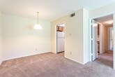 Located in Savannah, GA (31419), this single-floor unit offers a practical and straightforward layout designed for comfortable everyday living. The living area is generously sized, featuring wall-to-wall carpeting, neutral cream-toned walls, and a large sliding glass door that floods the space with natural light and provides a pleasant view of the surrounding greenery. A pendant light fixture anchors the dining area just off the main living space, adding a functional touch to the open feel of the floor plan.

The kitchen is equipped with wood-grain cabinetry that extends to the upper and lower sections of the walls, offering ample storage. White appliances, including a coil electric range and a full-size refrigerator, are complemented by white countertops and a stainless steel sink. The kitchen floor features tile, providing a practical contrast to the carpeting throughout the rest of the unit.

A hallway connects the living areas to the bedrooms, each of which features soft carpeting, neutral walls, ceiling light fixtures with fan pulls, and windows that bring in natural light and outdoor views. The bathroom includes a full tub-shower combination with clean white tile surround, maintaining a simple and functional aesthetic throughout the space.