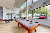 Located at 131 Ponce de Leon Ave NE in Atlanta, GA, this single-floor amenity space offers a generously sized, open-plan layout designed for both socializing and productivity. The architecture is defined by soaring double-height ceilings and expansive floor-to-ceiling windows that flood the interior with natural light and frame views of the surrounding urban streetscape and mature trees.

Light hardwood flooring runs throughout, complementing the clean white walls and contemporary finishes. The main gathering area serves as a versatile lounge and recreation hub, anchored by a full-size billiards table and two octagonal game tables surrounded by modern chairs — ideal for casual interaction and entertainment.

A curved bar-height communal table with upholstered stools serves as a central social and co-working surface, lit overhead by striking Sputnik-style pendant fixtures. Built-in shelving with curated décor accents and a textured blue accent wall add warmth and visual interest. A dedicated business center offers workstations equipped with desktop computers for resident use.

A glass-partitioned private conference or office room provides a quiet workspace separated from the open lounge. The reception area features marble-clad columns, a front desk, and a welcoming seating arrangement, completing a well-appointed, multi-functional community amenity environment.