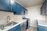 Located at 1201 S Courthouse Rd in Arlington, VA, this two-bedroom, one-bathroom unit offers a well-organized single-floor layout. The kitchen is a standout feature, equipped with bold navy blue cabinetry, quartz countertops, stainless steel appliances including a gas range, microwave, dishwasher, and refrigerator, and light wood-style flooring. A pass-through counter connects the kitchen to the adjacent living area, enhancing the open feel of the space.

The living room is bright and airy, featuring large windows that allow generous natural light and offer views of the surrounding Arlington cityscape. Light wood-style flooring continues throughout the main living area, complementing the neutral wall tones.

Both bedrooms are carpeted and receive natural light through multiple windows with views of the city. The primary bedroom is spacious, featuring a closet and room for a comfortable furniture arrangement. The second bedroom also offers closet storage and windows.

The bathroom is finished with white tile wainscoting, a white vanity with a modern faucet, a large mirror with overhead lighting, and tile flooring, presenting a clean and functional design throughout.