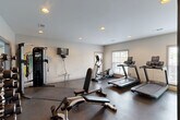 Located at 4025 Oakwood Dr in Chattanooga, TN, this single-floor facility is purpose-built to support both fitness and productivity. The space is divided into two functional areas: a well-appointed exercise room and a dedicated office.

The exercise room is the centerpiece of this facility, finished with durable rubber flooring ideal for high-impact activity. It is outfitted with multiple treadmills, an elliptical trainer, a multi-station cable machine, a weight bench, a dumbbell rack, and a medicine ball storage unit with an assortment of kettlebells and stability balls — providing a comprehensive range of cardio and strength training options. A wall-mounted flat-screen TV adds convenience for entertainment during workouts. Recessed lighting throughout ensures a bright, evenly lit environment, while multiple windows along the walls allow natural light to fill the space and offer views of the surrounding greenery.

The adjacent office is a clean, simply finished room featuring neutral walls, carpeted flooring, and a large window fitted with blinds that brings in ample natural light. The room provides a quiet, functional setting suitable for administrative tasks or study.

Together, these two rooms form a compact yet highly functional facility designed to serve the practical wellness and workspace needs of its users.