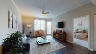 This single-floor residence offers a thoughtfully designed layout with a variety of well-defined living spaces. The living room serves as the centerpiece, featuring dark hardwood-style flooring, crown molding, a textured ceiling, and a ceiling fan with light fixture. Multiple windows, including a glass door leading to a private balcony, flood the space with natural light. A corner seating area with large windows enhances the open, airy feel.

The entryway transitions smoothly into a dedicated dining area, finished with tile flooring and track lighting overhead. Adjacent to it, the kitchen is well-equipped with stainless steel appliances, warm wood cabinetry extending to the ceiling, granite countertops, a tile backsplash, and a double sink.

The primary bedroom features plush carpeting, a sliding glass door opening to an outdoor balcony, and generous natural light. A secondary bedroom offers carpeted flooring, a bright window with sheer curtains, and wall space for artwork. The bathroom includes tile flooring, a wood vanity with granite countertop, and a tub-shower combination. Neutral tones and crown molding carry throughout, lending the space a cohesive and polished character.