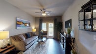 This single-story residence at 7938 City Base Landing in San Antonio, Texas, offers a well-appointed layout finished with consistent dark hardwood-style flooring throughout the main living areas and rich carpet in the bedrooms. The inviting living room features a ceiling fan, neutral-toned walls, and large sliding glass doors that open to a private patio, allowing natural light to fill the space. A decorative media cabinet and colorful abstract artwork add character to the room.

The kitchen is equipped with warm-toned wood cabinetry, granite-style countertops, a mosaic tile backsplash, and black appliances including a refrigerator, range, and dishwasher. A kitchen island with a sink provides added workspace, while an adjacent dining area accommodates casual meals.

The bedrooms offer a serene retreat with plush carpeting, ceiling fans, and windows that bring in natural light. Each room provides comfortable proportions suited for restful living.

The bathrooms are finished with rich wood vanities topped with granite-style counters, large mirrors with lighted fixtures, and tub-shower combinations with tile surrounds and dark hardwood-style flooring, maintaining a cohesive design throughout.

Overall, the residence presents a warm and cohesive aesthetic with thoughtful finishes and a practical, comfortable floor plan.