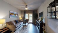 This single-story residence at 7938 City Base Landing in San Antonio, Texas, offers a well-appointed layout finished with consistent dark hardwood-style flooring throughout the main living areas and rich carpet in the bedrooms. The inviting living room features a ceiling fan, neutral-toned walls, and large sliding glass doors that open to a private patio, allowing natural light to fill the space. A decorative media cabinet and colorful abstract artwork add character to the room.

The kitchen is equipped with warm-toned wood cabinetry, granite-style countertops, a mosaic tile backsplash, and black appliances including a refrigerator, range, and dishwasher. A kitchen island with a sink provides added workspace, while an adjacent dining area accommodates casual meals.

The bedrooms offer a serene retreat with plush carpeting, ceiling fans, and windows that bring in natural light. Each room provides comfortable proportions suited for restful living.

The bathrooms are finished with rich wood vanities topped with granite-style counters, large mirrors with lighted fixtures, and tub-shower combinations with tile surrounds and dark hardwood-style flooring, maintaining a cohesive design throughout.

Overall, the residence presents a warm and cohesive aesthetic with thoughtful finishes and a practical, comfortable floor plan.