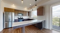 This contemporary single-floor residence offers a thoughtfully designed open-concept layout that seamlessly connects the kitchen and living area. The kitchen is a standout feature, showcasing two-tone dark cabinetry, crisp white quartz countertops, a classic subway tile backsplash, and a full suite of stainless steel appliances including a gas range, microwave, dishwasher, and refrigerator. A peninsula with pendant lighting provides additional prep space and serves as a natural divider between the kitchen and the expansive living area. Rich wood-look flooring runs throughout the main living spaces, while large windows and a sliding glass door lead to a private balcony, flooding the area with natural light and offering sweeping outdoor views.

The bedrooms are carpeted for comfort and each include ceiling fans and generous windows that frame views of the surrounding cityscape and greenery. Two full bathrooms are finished with dark wood vanities, white quartz countertops, large mirrors, and clean white tile surrounds in the tub and shower areas. One bathroom features wood-look flooring, while the other offers a more compact, efficient layout. Overall, the unit presents a clean, modern aesthetic with well-coordinated finishes and a bright, airy ambiance throughout.
