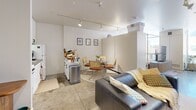 Located at 255 Iowa Ave in Iowa City, Iowa, this studio unit offers a thoughtfully arranged open-concept floor plan across a single level. The main living area features polished concrete floors, bright white walls, and a sleek track lighting system that runs throughout, providing both functional illumination and a modern industrial aesthetic. Large windows allow natural light to fill the space and offer views of the surrounding urban streetscape.

The open layout seamlessly connects the living, sleeping, and dining zones. The sleeping area accommodates a four-poster bed frame and includes ample wardrobe storage, while the living area provides room for a sofa, media console, and shelving units. A compact dining nook with a glass table sits adjacent to the kitchenette, which is equipped with essential appliances including a refrigerator and range.

The bathroom is efficiently designed with a pedestal sink paired with a lighted vanity mirror, a toilet, and a shower with a curtain enclosure. Warm wood-toned storage units maximize organization within the space. Clean white walls and neutral flooring maintain a cohesive, minimalist feel throughout. This unit offers a practical and contemporary living environment well-suited for single occupancy in the heart of Iowa City.
