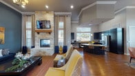 Located at 11211 Westwood Loop in San Antonio, TX, this single-story community clubhouse offers a well-appointed and thoughtfully designed gathering space. The entry foyer welcomes visitors with warm hardwood flooring, accent walls in bold yellow and gray tones, and curated artwork that sets an inviting atmosphere throughout.

The reception area features a curved granite-topped workstation with dark cabinetry, pendant lighting, and direct access to an outdoor patio through glass French doors, allowing natural light to pour in. Deep blue accent walls and abstract artwork lend the space a professional yet comfortable character.

The central lounge is a standout, boasting soaring vaulted ceilings, a dramatic floor-to-ceiling stacked stone fireplace with a wood mantel, and a wall-mounted television. Expansive windows dressed with layered drapes flood the room with natural light, while richly colored furnishings in navy and gold complement the warm hardwood floors.

Adjacent to the lounge, the open kitchen and dining area is equally impressive. Dark cabinetry, a large center island with granite countertops and bar seating, stainless steel appliances, and abundant window views make this a functional and attractive communal space. A separate dining area with a chandelier and generous natural light completes this inviting clubhouse.