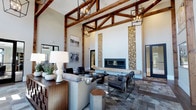 Located at 1800 Indigo Square in Mount Pleasant, South Carolina, this single-story space makes a striking architectural statement through its combination of rustic charm and contemporary sophistication. The main living area commands immediate attention with its soaring vaulted ceiling, where rich, dark-stained wooden trusses create a dramatic framework against crisp white walls. Pendant lantern-style chandeliers with an industrial edge hang from the ceiling, casting warm, inviting light throughout the space.

The focal point of the room is a sleek, linear fireplace set into a bold white accent wall, flanked by floor-to-ceiling displays of stacked firewood that serve as both a functional storage solution and a striking design feature. The hearth is finished with a clean, contemporary surround that balances the rustic overhead elements.

The interior is furnished with a curated mix of upholstered seating in neutral tones, leather accent chairs with metal frames, and wooden side tables, creating a refined yet approachable atmosphere. The flooring features geometric patterned tile that adds visual texture and depth. Natural light filters into the space, enhancing its open, airy ambiance, while French doors provide a seamless connection to the exterior.