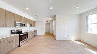 Located at 1023 Westwind St in Livermore, California, this single-floor unit offers a clean, contemporary design throughout. Light-toned hardwood-style flooring runs seamlessly across the open-concept living and kitchen areas, creating a cohesive and airy atmosphere brightened by recessed lighting overhead.

The kitchen is well-appointed with warm wood-grain cabinetry extending to the ceiling, offering generous storage on both upper and lower levels. Stainless steel appliances — including a refrigerator, electric range, over-the-range microwave, and dishwasher — complement the crisp white countertops and single-basin sink, making the space as functional as it is visually appealing.

The living area is notably bright, with a bank of windows along one wall inviting abundant natural light and views of the surrounding neighborhood. The open layout allows for versatile furniture arrangements and a comfortable sense of spaciousness.

The bathroom is finished in a clean, minimalist style, featuring a combined tub and shower unit with built-in shelving, a wood-accented vanity with a white countertop, and matching light flooring. The walk-in closet provides substantial storage, outfitted with wire shelving and carpeted flooring for added comfort. A connecting hallway ties each area of the unit together, contributing to a practical and well-organized floor plan.