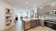 Located at 99 Wilkens Lane in Barnstable, MA, this thoughtfully designed single-floor residence offers a cohesive blend of modern aesthetics and functional living. The open-concept kitchen and living area serves as the heart of the home, where wood-look flooring, recessed lighting, and crisp white ceilings create a bright, welcoming atmosphere. The kitchen is outfitted with contemporary wood-grain cabinetry, a stainless steel appliance suite including a refrigerator, range, microwave, and dishwasher, and a peninsula with a white quartz countertop and undermount sink — ideal for both cooking and casual dining. A subtle tile backsplash adds texture to the kitchen wall. The living area is anchored by floor-to-ceiling windows with blinds and sheer curtains that invite an abundance of natural light and provide access to an outdoor area, enhancing the sense of openness. The bathroom features marble-look tile flooring, a floating vanity with quartz countertop, a large mirror, wood-grain wall cabinet, and a tub-shower combination, delivering a clean and spa-like aesthetic. A dedicated closet provides practical storage. Throughout the space, the design palette of neutral tones, modern fixtures, and quality finishes creates a polished and comfortable living environment.