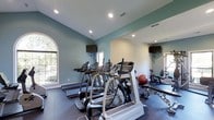 Located at 5300 New Center Dr in Wilmington, NC, this fitness center offers a well-appointed, single-floor workout facility designed to support a well-rounded exercise routine. The space is finished with soft sage-green walls and durable rubber flooring, creating a clean and energizing environment conducive to focused training.

The cardio section is well-equipped with multiple treadmills and elliptical machines, all arranged to maximize usable floor space. Wall-mounted flat-screen televisions are positioned throughout the room, allowing members to stay entertained during workouts. The strength and functional training area includes free weights, a stability ball, and resistance machines, providing a comprehensive range of exercise options.

Natural light flows in through large arched windows, giving the space an open and inviting feel. Recessed ceiling lighting supplements the natural light, ensuring the facility is well-lit at all times of day. Full-length mirrors line one wall, enhancing the sense of space while serving a practical purpose for form and technique.

The layout is thoughtfully organized, with distinct zones for cardio and strength training that allow multiple users to exercise simultaneously without crowding. The overall ambiance is clean, modern, and functional — making this fitness center a convenient and effective amenity.
