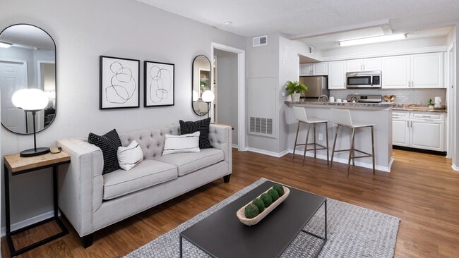 Enjoy the inviting feel of this open-concept living area featuring wood-style flooring, modern finishes, and a seamless flow into the kitchen—perfect for hosting or relaxing. - The Oasis at 1800