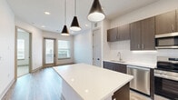 Located at 9001 Metcalf Ave in Overland Park, Kansas, this thoughtfully designed one-bedroom, one-bathroom residence offers a modern aesthetic with high-quality finishes throughout. The open-concept kitchen is a standout feature, showcasing dark espresso cabinetry, a white quartz waterfall island, a white subway tile backsplash, and a full suite of stainless steel appliances including a refrigerator, range, microwave, and dishwasher. Light wood-look flooring runs throughout the main living areas, complementing the clean, neutral color palette and recessed pendant lighting. A door leads to a private balcony, with an adjacent window inviting natural light into the living area and offering outdoor views. The bedroom is a comfortable retreat finished with plush carpet, a ceiling fan, and a large window framing views of the surrounding area. The bathroom is well-appointed with a dark wood vanity, white countertop, wood-look tile flooring, and a glass-enclosed tub and shower adorned with elegant marble-style tile. A dedicated closet completes the layout, providing practical storage. The overall ambiance is clean, contemporary, and move-in ready.