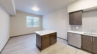 Located in Tumwater, Washington, this thoughtfully designed one-bedroom, two-bathroom residence offers a smart and functional layout with modern finishes throughout. The open-concept kitchen and living area serves as the heart of the home, featuring light wood-look flooring, a central island with a white countertop and dark cabinetry, and a bright window that fills the space with natural light. The kitchen is fully equipped with stainless steel appliances — including a refrigerator, range, microwave, and dishwasher — complemented by rich dark wood shaker-style cabinetry and a classic gray subway tile backsplash with recessed lighting above. A hallway connects the main living area to the private bedroom, which is carpeted for comfort and includes a large window with outdoor views and access to a spacious walk-in closet outfitted with wire shelving. The unit includes four closets in total, offering generous storage throughout. One bathroom features a dark vanity with a white countertop alongside a stacked washer and dryer, adding convenient in-unit laundry. Consistent dark trim accents frame doorways and windows across the residence, lending a polished, cohesive aesthetic to this move-in-ready Tumwater home.