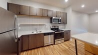 This single-floor unit offers a clean, contemporary design with a cohesive aesthetic carried throughout each room. The kitchen serves as a functional centerpiece, showcasing rich dark-toned cabinetry that extends to the ceiling, stainless steel appliances including a refrigerator, range, microwave, and dishwasher, and light granite-style countertops. A white subway tile backsplash adds a modern touch, while a central island provides additional prep space and casual seating. Warm, light-toned hardwood flooring runs throughout the main living areas, contributing to a bright and welcoming atmosphere.

The bedroom is a calm, neutral space featuring plush wall-to-wall carpeting for added comfort. A large window floods the room with natural light and offers views of the surrounding area, making the space feel open and airy.

The bathroom is well-equipped with a soaking tub and shower combination, a wide vanity with dark wood cabinetry and ample drawer storage, a large mirror with overhead lighting, and a matching tall storage cabinet. The continuation of hardwood flooring into the bathroom ties the space together seamlessly.

Overall, this unit presents a thoughtfully designed interior that balances modern style with practical functionality, making it a comfortable and move-in-ready space.